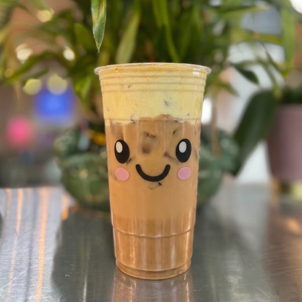 Iced coffee with a creamy foam topping and a cute smiling face sticker on the cup.