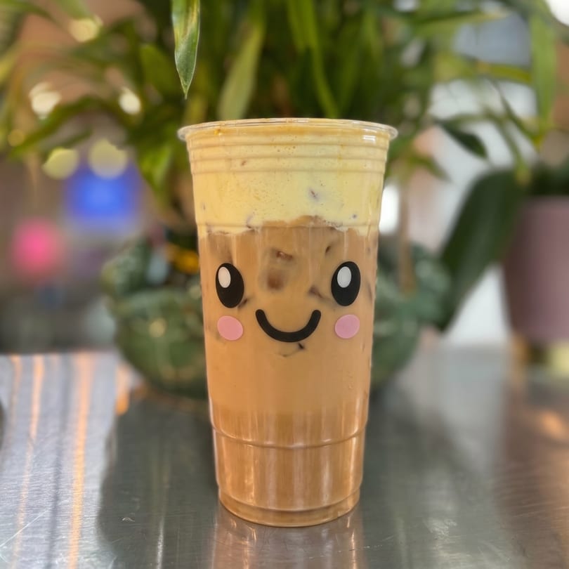 Iced coffee with a creamy foam topping and a cute smiling face sticker on the cup.