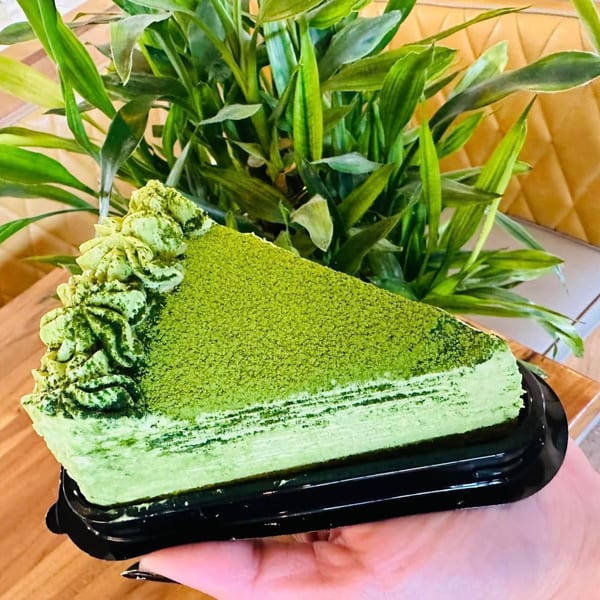 Hand holding a slice of green matcha crepe cake with whipped cream and matcha powder.