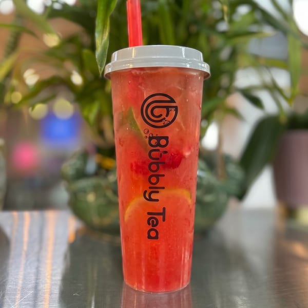 A vibrant red Bubbly Tea drink with fruit slices and a red straw sits on a metallic surface.
