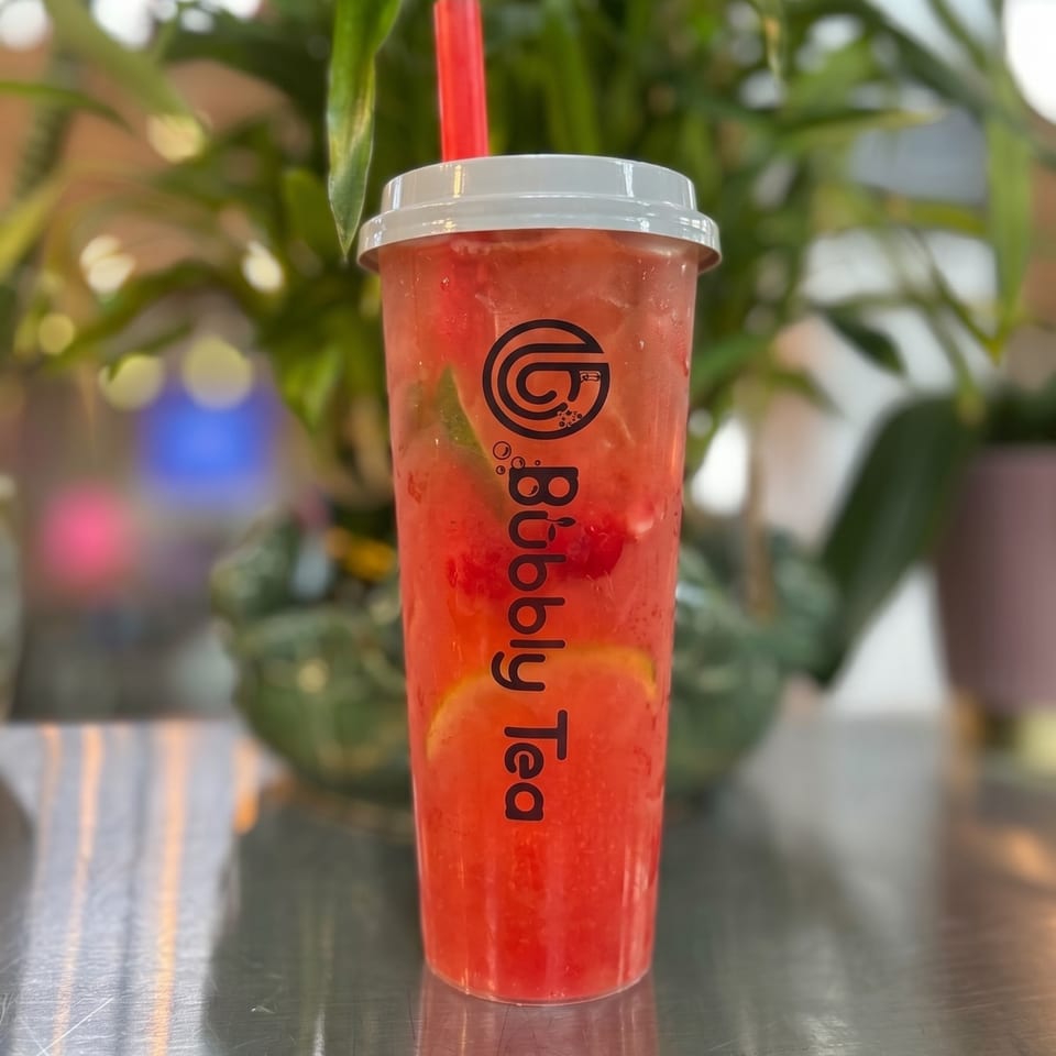 A vibrant red Bubbly Tea drink with fruit slices and a red straw sits on a metallic surface.