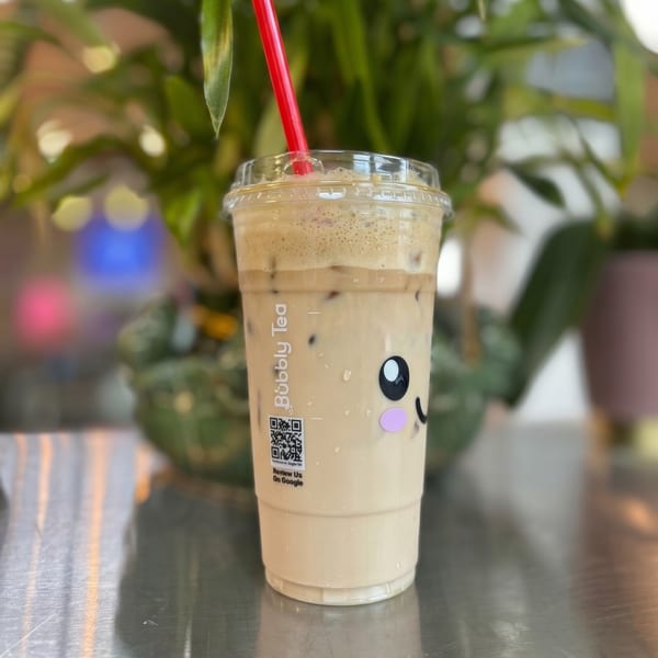 Bubbly Tea drink with a cute face logo, red straw, and QR code on a metallic surface.