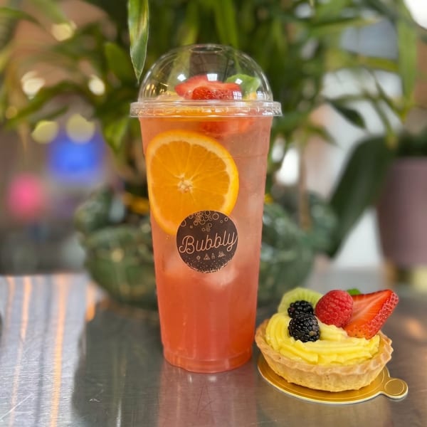 A Bubbly brand fruit drink with an orange slice and a fruit tart on a metallic surface.