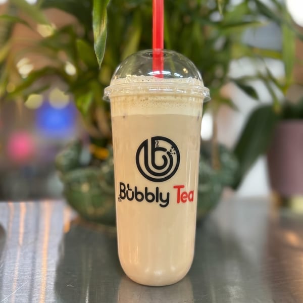 A Bubbly Tea branded cup of light brown bubble tea with a red straw on a reflective surface.