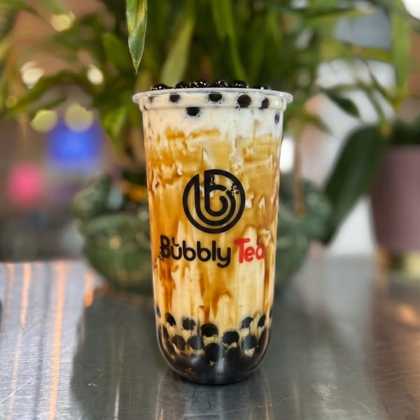 A Bubbly Tea brown sugar boba drink with creamy white foam and dark pearls on a metallic surface.