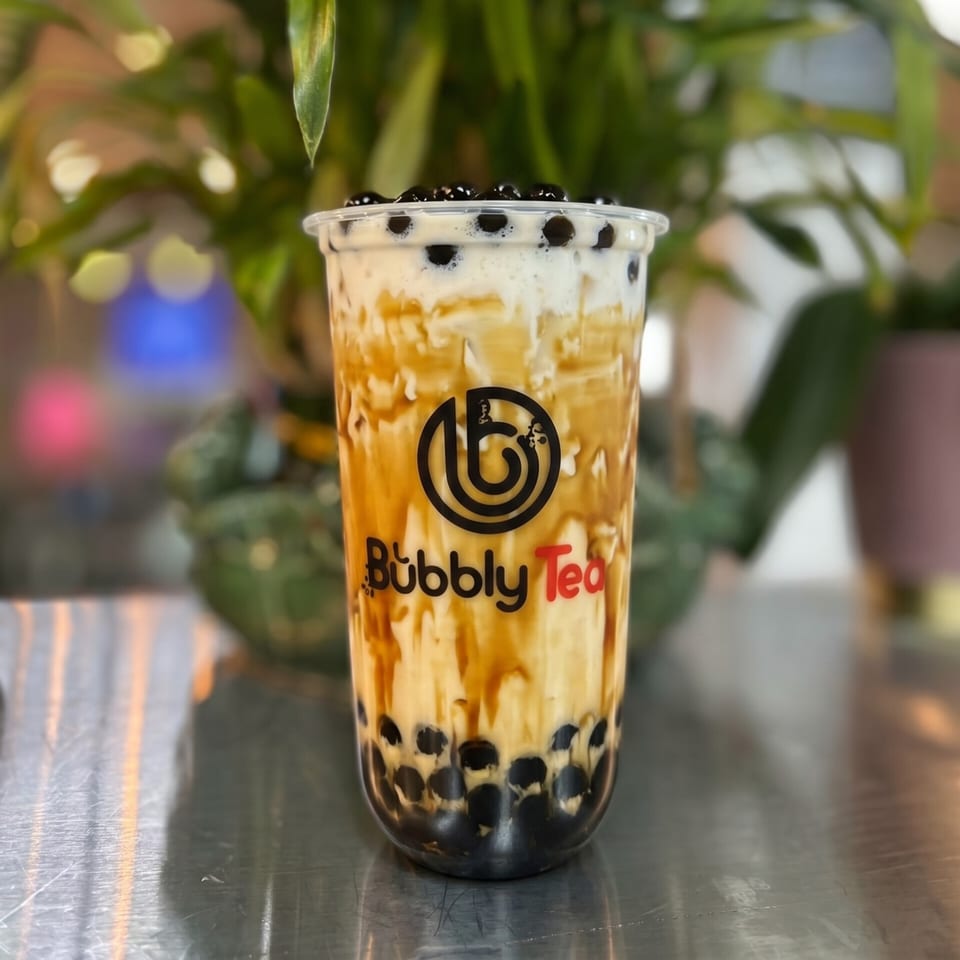 A Bubbly Tea brown sugar boba drink with creamy white foam and dark pearls on a metallic surface.